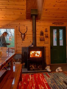 a woman standing next to a wood stove in a room filled with wooden floors and walls