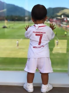 a young boy standing on top of a window sill looking out at a soccer field