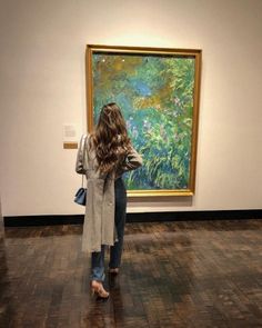 a woman standing in front of a painting looking at it's reflection on the floor