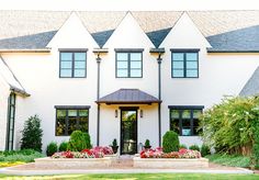 a large white house with lots of windows and flowers in the front yard, on a sunny day