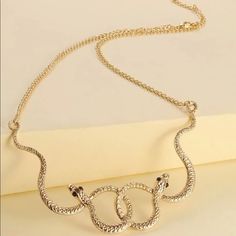 a gold necklace with two snakes hanging from it's center, on a white surface