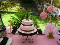 a pink table topped with a tiered cake next to flowers and other items on top of it