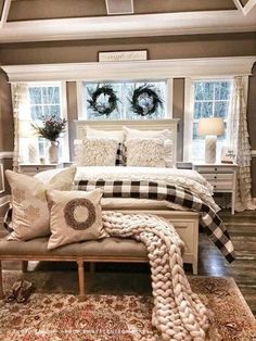 a white bed sitting in a bedroom next to two windows with wreaths on them