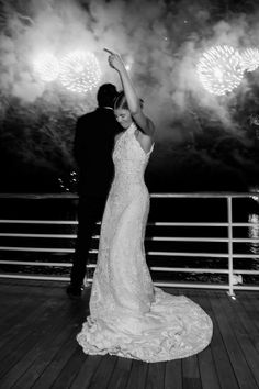 a bride and groom dance on the deck of a ship as fireworks go off in the background