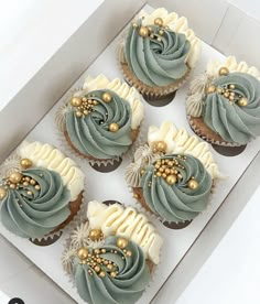 six cupcakes with frosting and gold decorations in a white box on a table