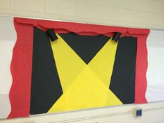 a large piece of art hanging on the wall in a school room with red, yellow and black colors