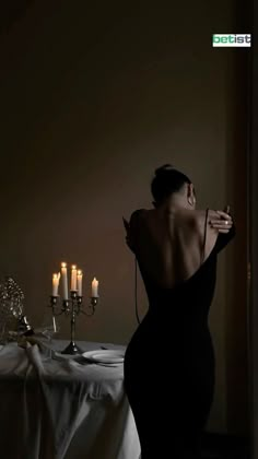 a woman in a black dress standing next to a table with candles on top of it