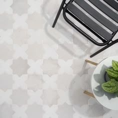 a bowl of basil next to a chair on a tile floor with white and gray tiles