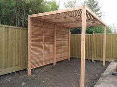 a wooden pergolated area in the middle of a fenced in area with trees