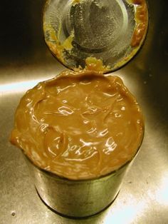 a cup filled with peanut butter sitting on top of a metal sink next to a spoon