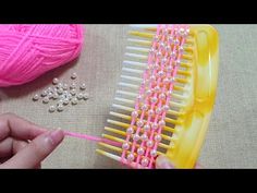 a person holding a pink comb next to a ball of yarn and beads on a table