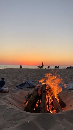 there is a fire pit on the beach with people in the background at sunset or dawn