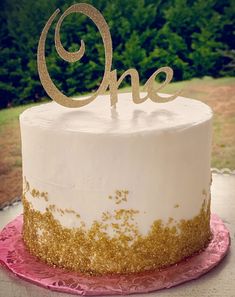 a white cake with gold sprinkles and the word one on top is sitting on a pink plate