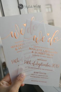 two white and gold wedding cards held up in front of a window with the words we do wed written on them