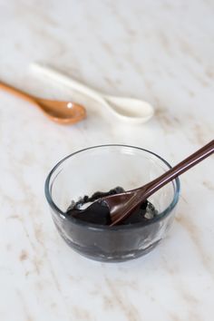 two spoons and a glass bowl filled with black liquid on a marble counter top