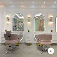 two salon chairs in front of mirrors with lights on the wall and floor below them