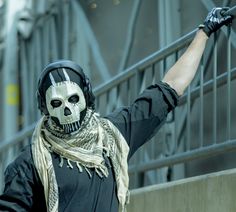 a man wearing a skeleton mask and scarf with his arms in the air while standing next to a railing