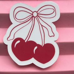 two cherries with a bow on top of pink background, one is white and the other is red