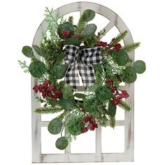 a christmas wreath with berries and greenery hanging on a white wooden door frame against a white background