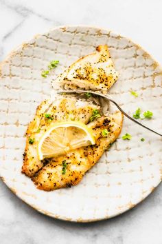 a white plate topped with chicken covered in lemon and parsley next to a fork