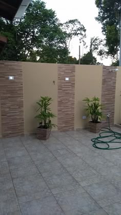 an outdoor area with plants and water hoses on the wall, in front of a fence