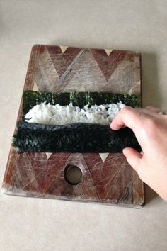 a person is cutting up sushi on a wooden board with white rice and greens