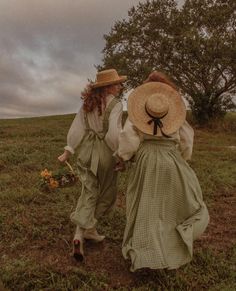 two women in dresses and hats walking through a field