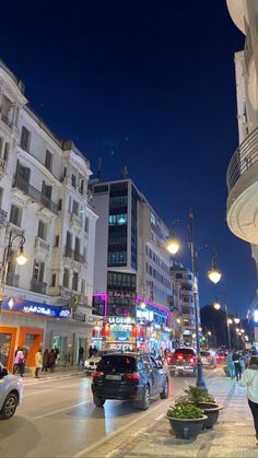 a city street at night with cars and people walking on the sidewalk, buildings in the background