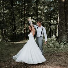 a bride and groom standing in the woods holding each other's hands up with their arms