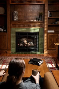 a person sitting on a couch in front of a fireplace with a book and cup