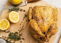 a whole chicken sitting on top of a cutting board next to lemons and herbs