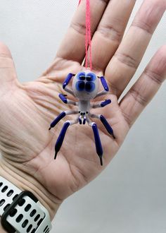 a hand holding a blue and white spider on it's palm with red string