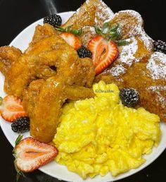 a white plate topped with fried chicken, scrambled eggs and fruit covered in powdered sugar