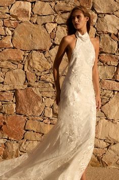 a woman standing in front of a stone wall wearing a white dress and high heels