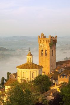 an old church tower in the middle of a foggy valley with trees around it