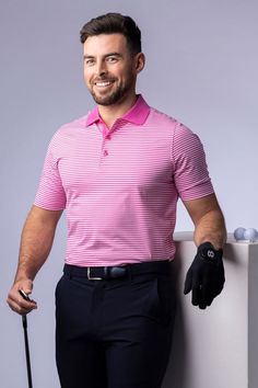 a man holding a golf club standing next to a white wall and smiling at the camera