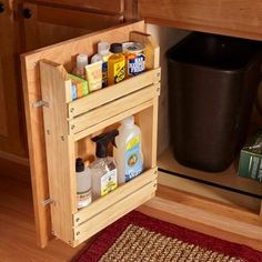 a wooden cabinet filled with cleaning products on top of a red rug next to a black trash can