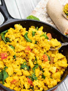 a skillet filled with yellow and red food on top of a white wooden table