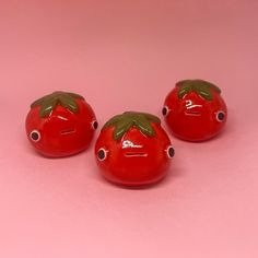 three small red tomatoes with green leaves on their heads, sitting next to each other