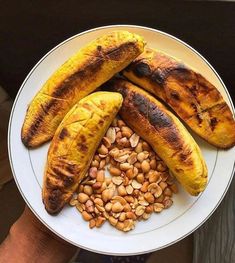 there is a plate with bananas and nuts on it, next to a person's hand