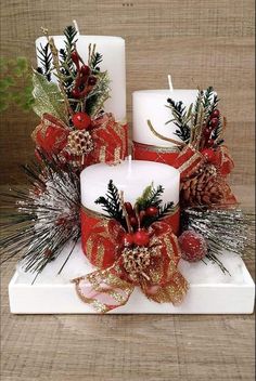 two white candles decorated with red and gold ribbons, pine cones, and evergreens