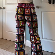 a woman wearing colorful crocheted pants standing in front of a door with her hands on her hips