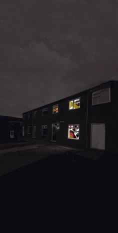 an empty street at night with some buildings lit up in the dark and stars above