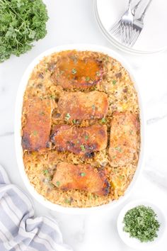 a white dish filled with meat and rice on top of a table next to silverware