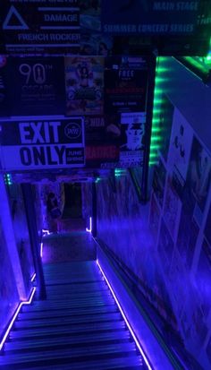 an escalator that is lit up with purple lights and advertisements on the wall