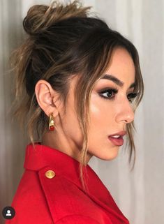 a woman wearing gold earrings and a red coat with her hair in a high bun