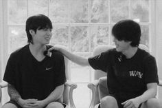 two young men sitting next to each other on chairs in front of a large window