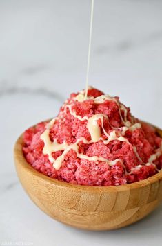 a wooden bowl filled with red cake and white icing on top of a table