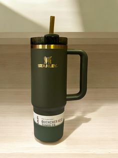 an army green travel mug with a gold lid and straw in it sitting on a wooden surface