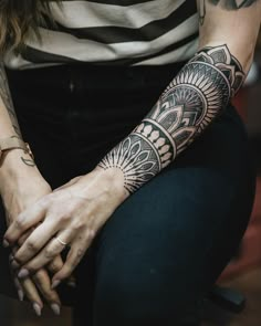 a woman with tattoos on her arm sitting down and holding her hands in front of her